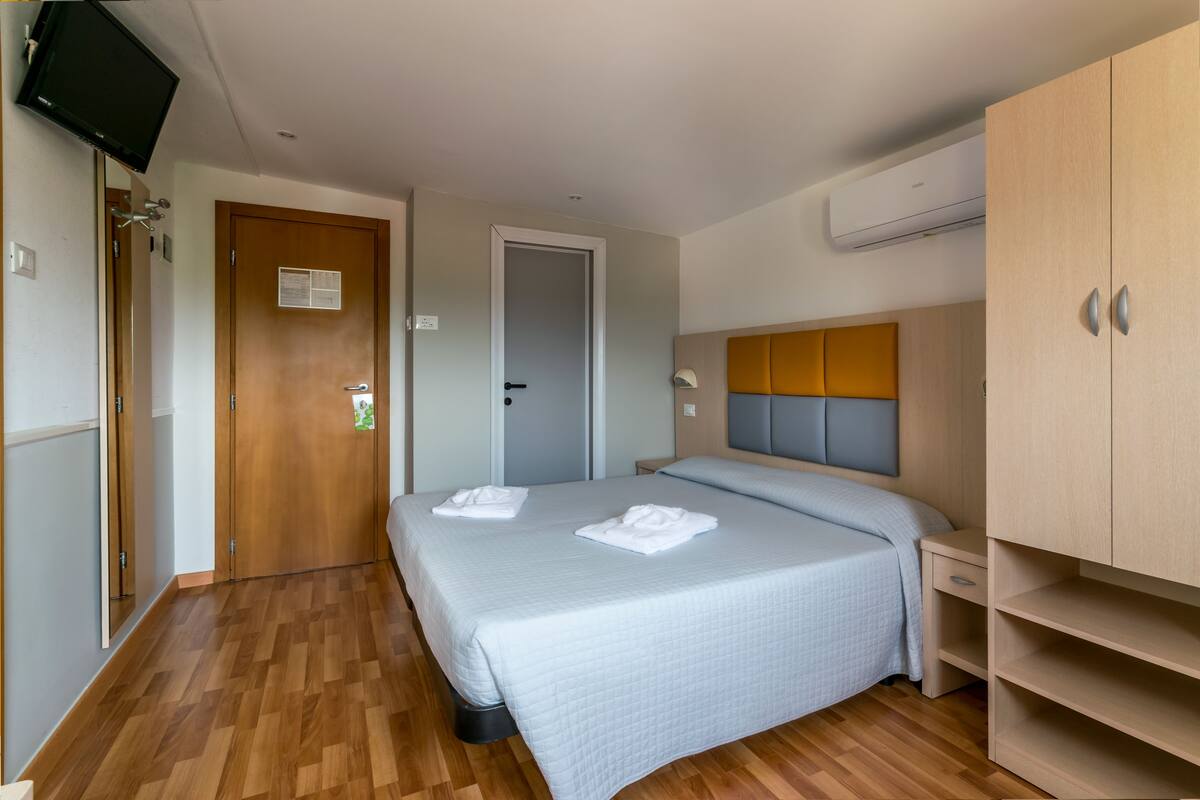 A hotel room with a bed, a wardrobe, a television, and an air conditioning unit.