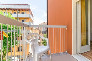 A balcony with a white plastic chair, a metal railing, and a view of neighboring buildings. - Hotel Stresa (Rimini)