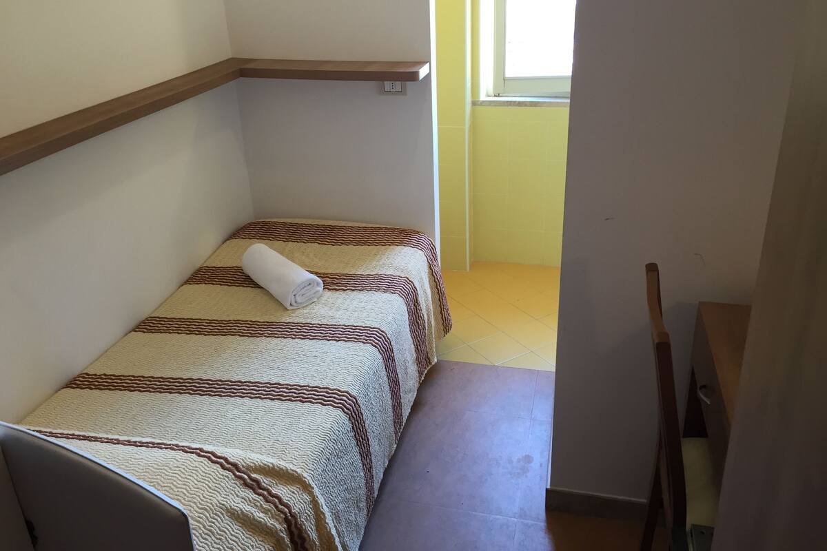 A small, narrow room with two beds, a bench, and a window.