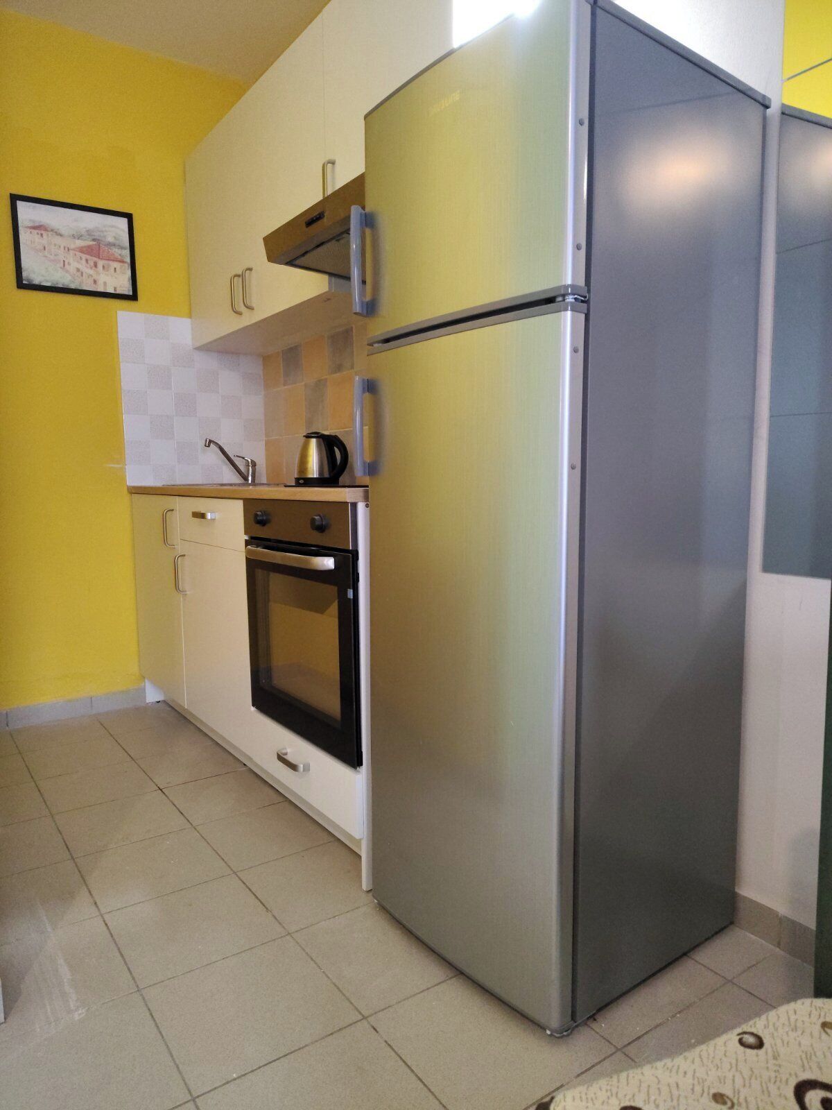 A compact kitchen with a stainless steel refrigerator, a built-in oven, and a sink.
