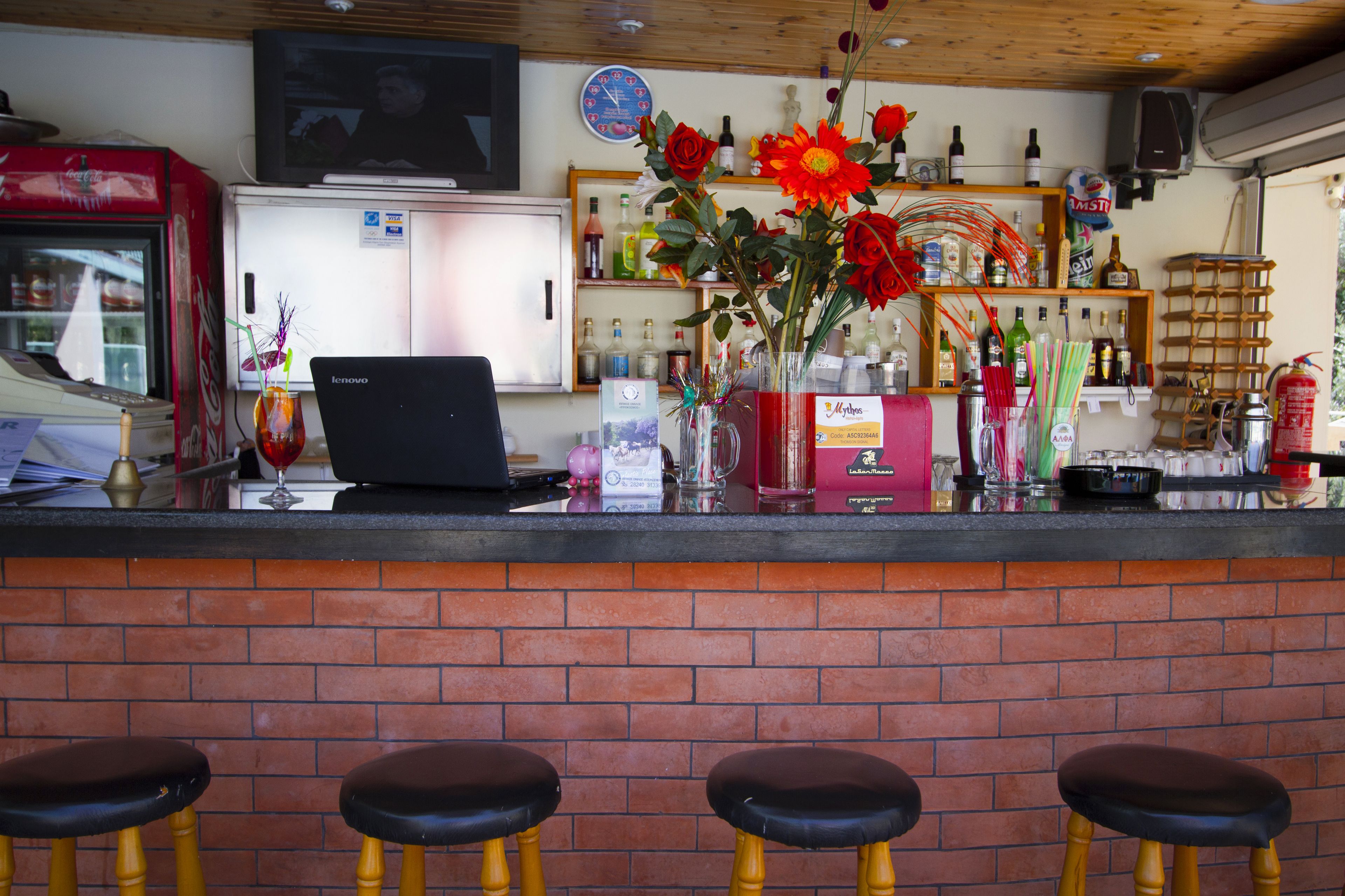 A bar area with a brick counter, a refrigerator, shelves with bottles, and three stools.
