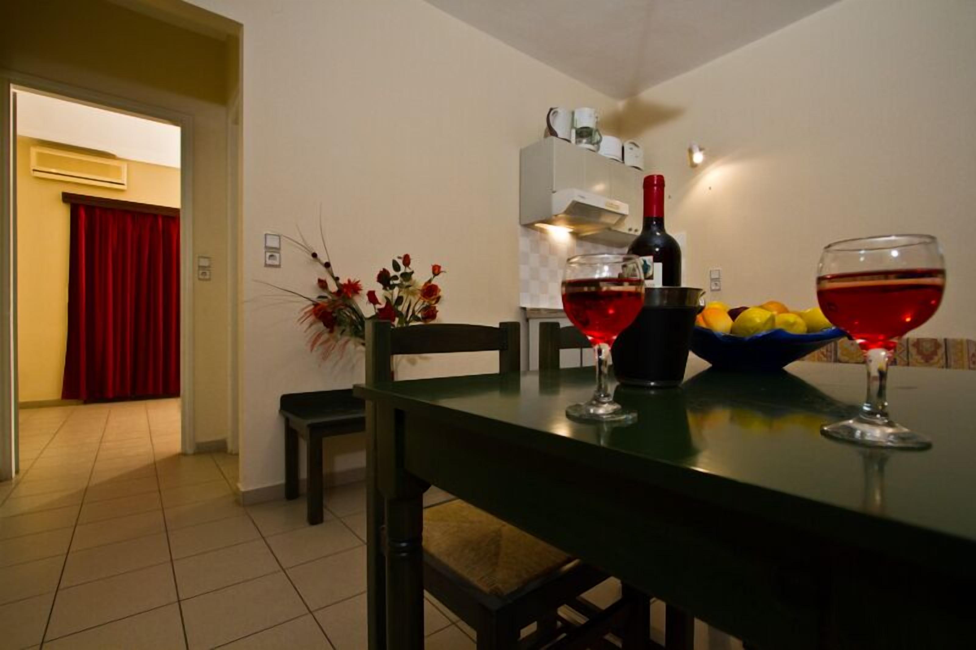 A dining area with a table set for two, a bottle of red wine, and a bowl of fruit.