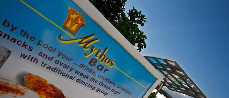 Señal del Mythos Bar que anuncia aperitivos, bebidas, cócteles, desayuno y una noche griega con un grupo de baile tradicional.