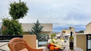 Una sedia in vimini con un cuscino su un tavolo da balcone, con una bottiglia di vino, bicchieri e frutta.