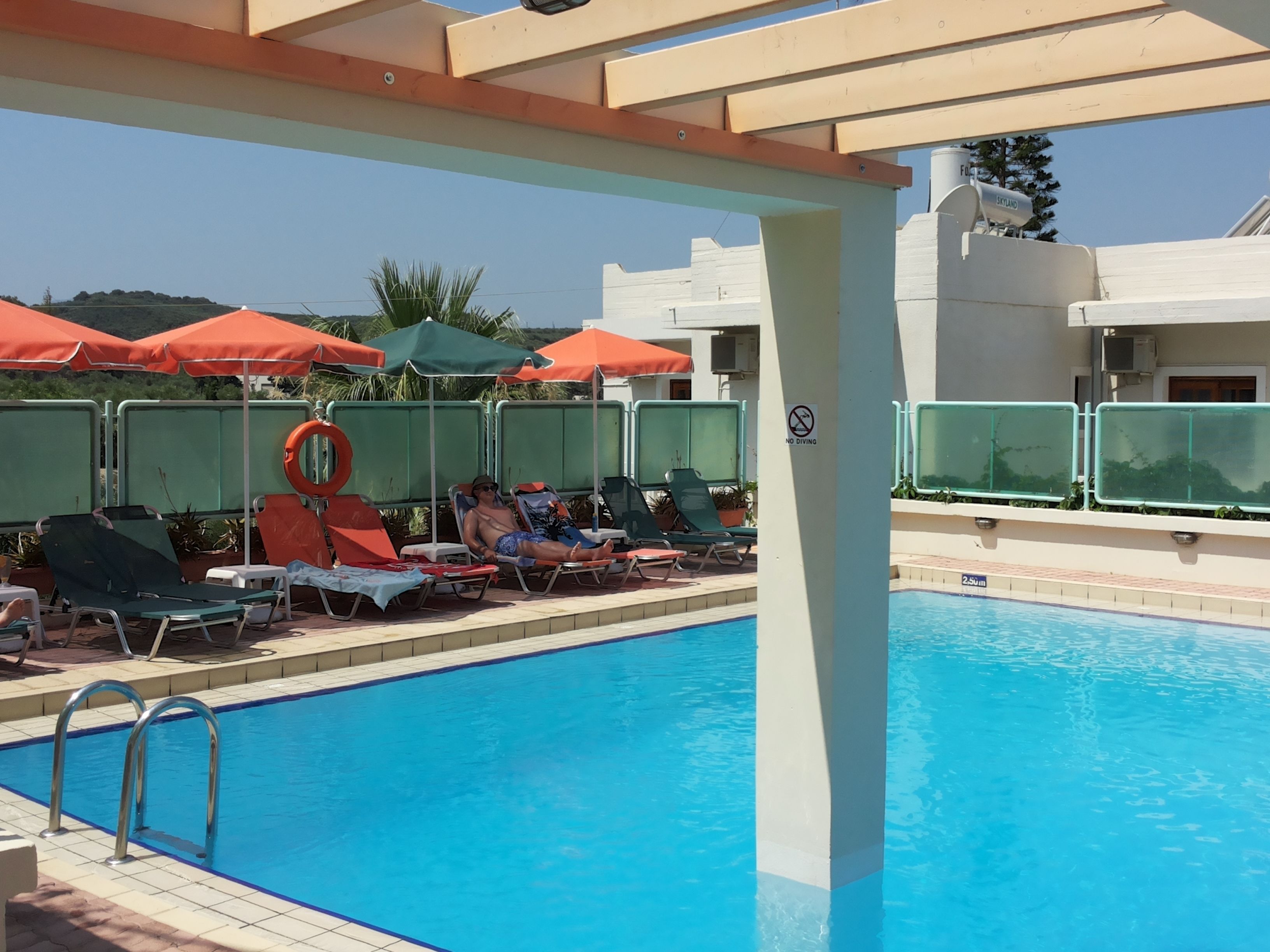 A pool area with lounge chairs and umbrellas, a no diving sign, and a clear blue pool.