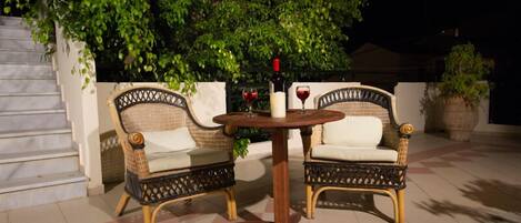 Un patio con sillas de mimbre y una mesa redonda, una botella de vino tinto y una copa de vino tinto.