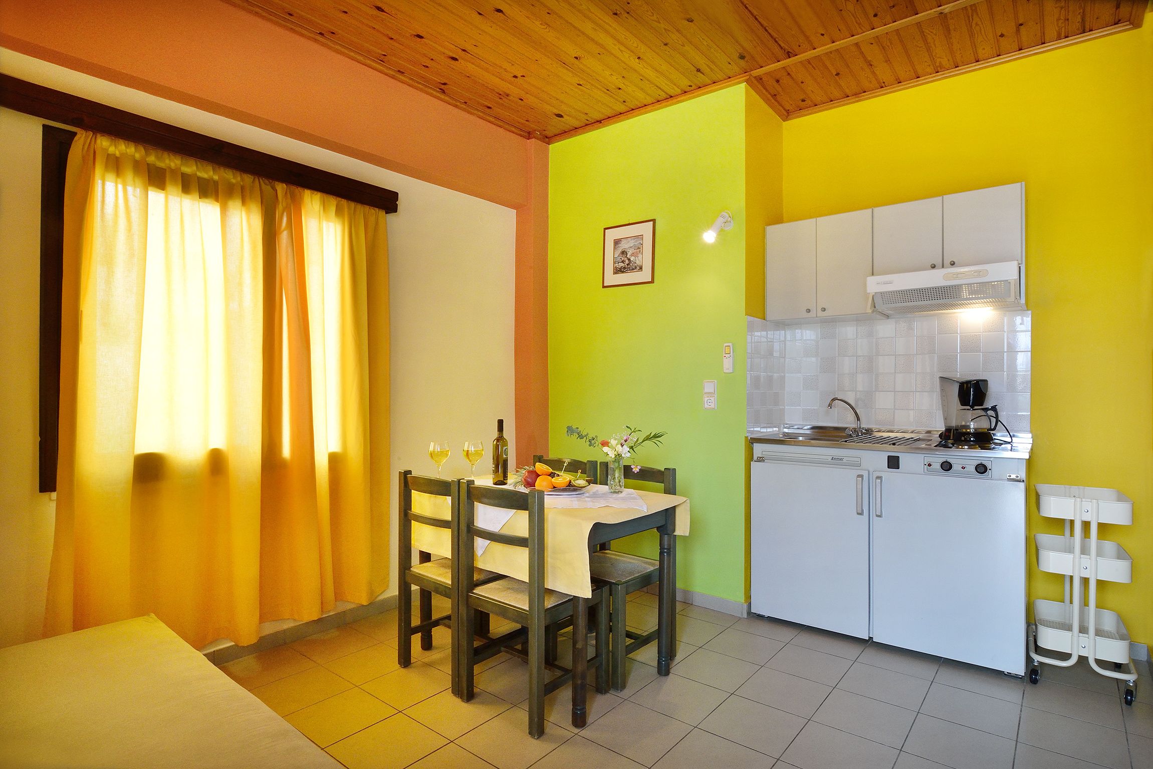 A compact kitchen with white cabinets, a dining table with chairs, and a yellow wall.