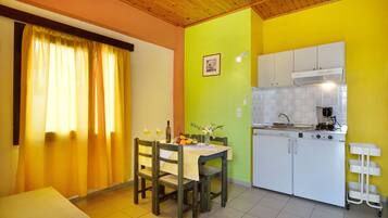A compact kitchen with white cabinets, a dining table with chairs, and a yellow wall.
