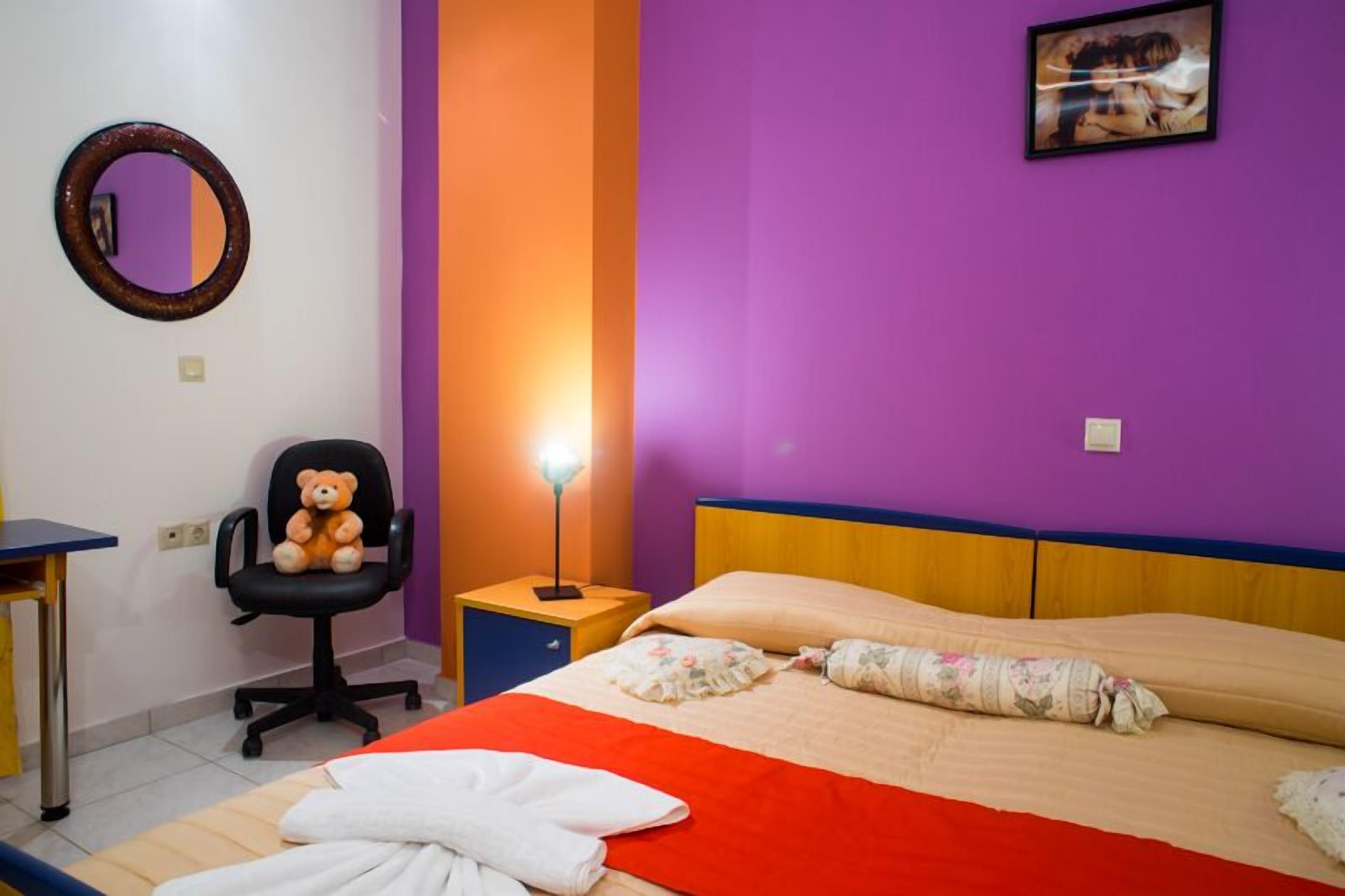 A bedroom with a bed, a chair, a bedside table, and a mirror.
