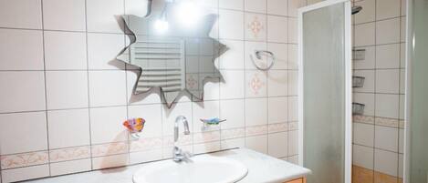 A bathroom with a white sink, a mirror with a unique design, and a shower area.