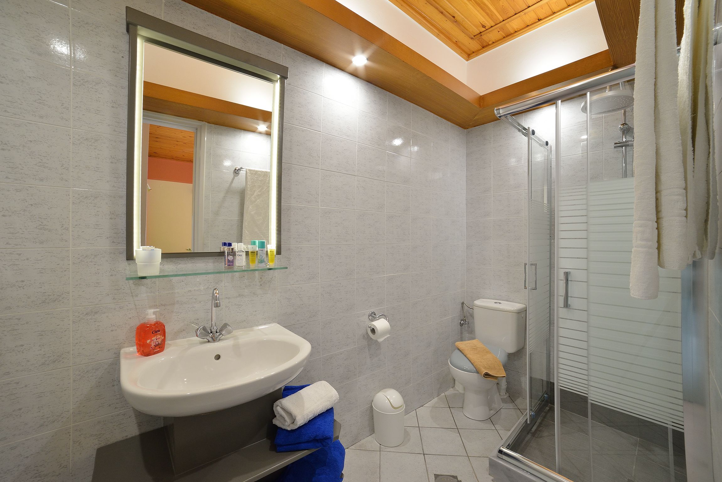 Un baño moderno con cabina de ducha de vidrio, un lavamanos blanco con estante de cristal y un inodoro con una toalla en el asiento.