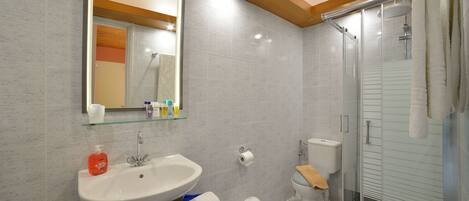 Un baño moderno con cabina de ducha de vidrio, un lavamanos blanco con estante de cristal y un inodoro con una toalla en el asiento.