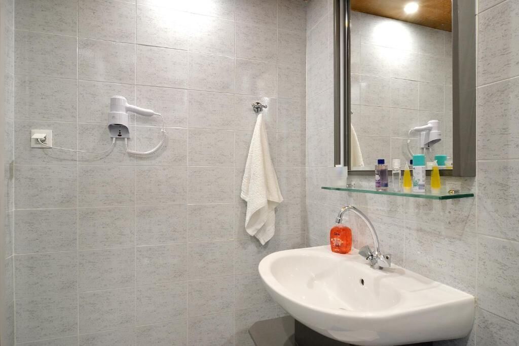 A bathroom with a white sink, a glass shelf with toiletries, a towel hanging on a hook, and a hairdryer mounted on the wall.