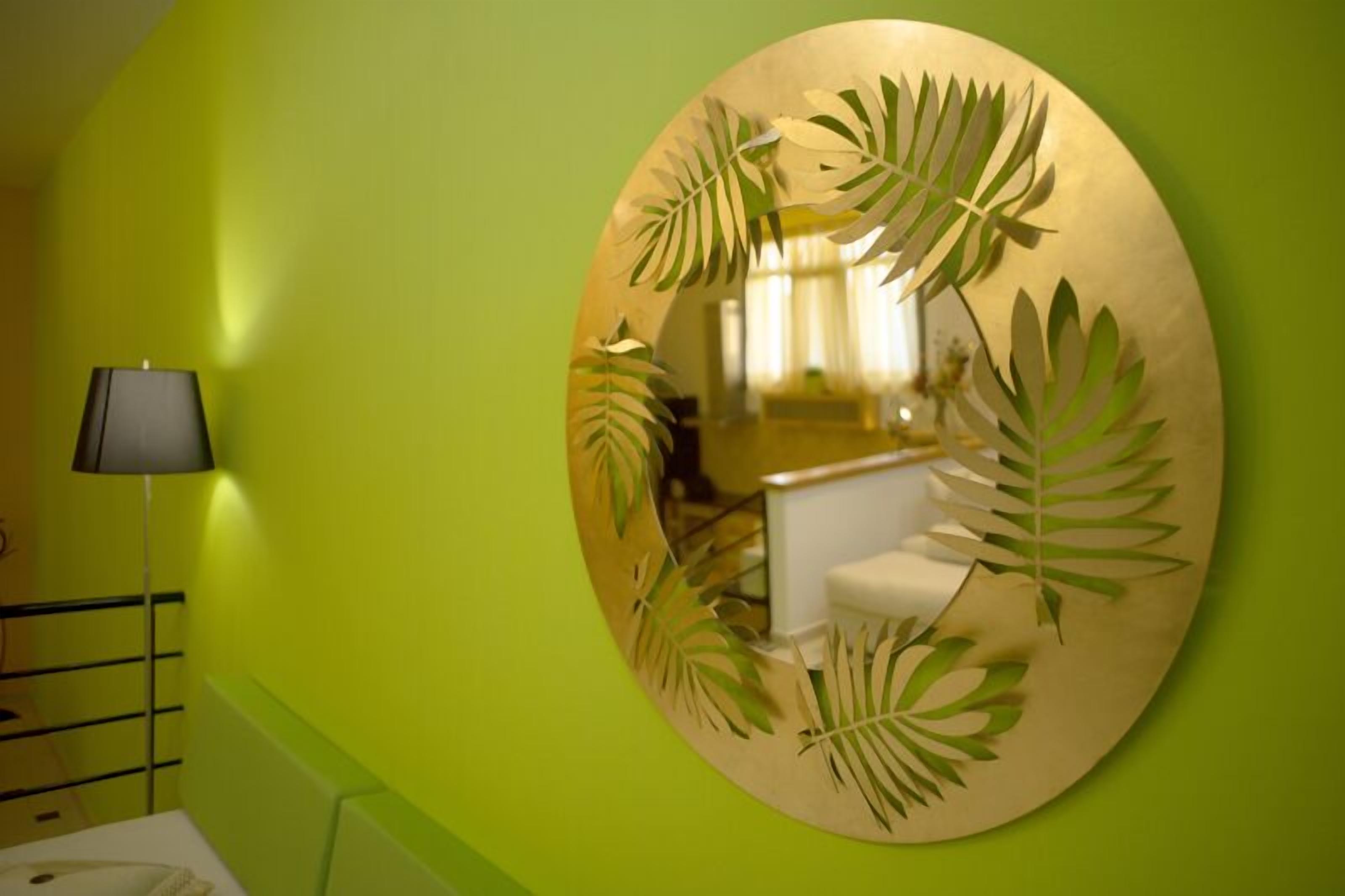 A bathroom with a green wall, a round mirror with leaf designs, and a black floor lamp.