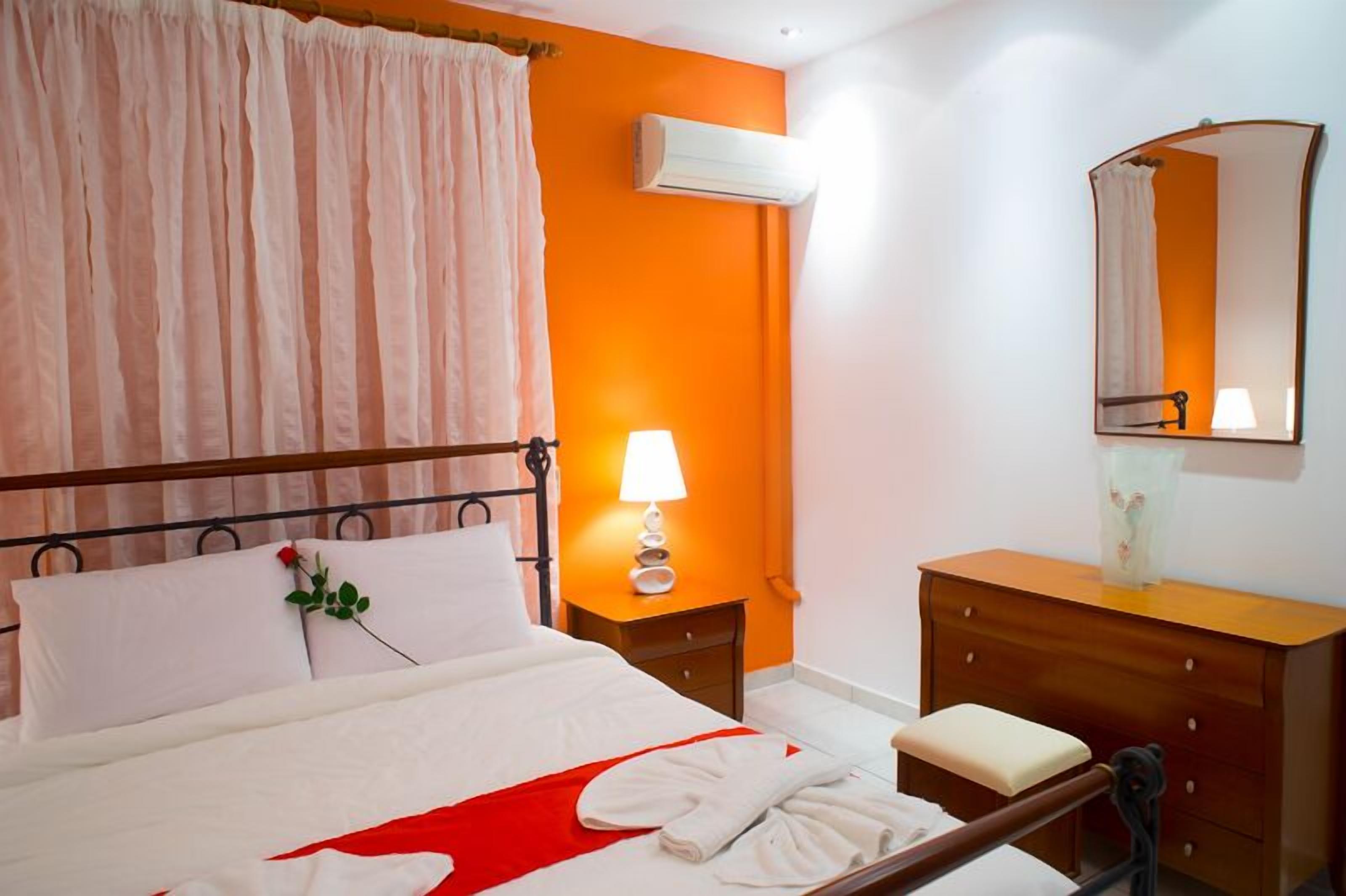 A hotel room with a bed, a bedside table with a lamp, a wooden dresser, and a mirror on the wall.