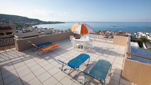 A rooftop terrace with a view of the sea, a table with chairs, and lounge chairs. - Memories Apartments (Hersonissos)