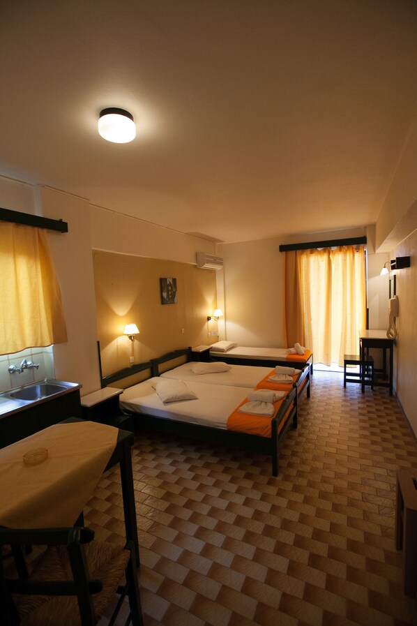 Une chambre d’hôtel avec trois lits simples, un bureau, une chaise, un lavabo et un miroir.