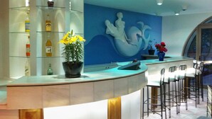 Un área de bar moderna con una barra curva, una planta en maceta con flores amarillas y un mural de una sirena en la pared.