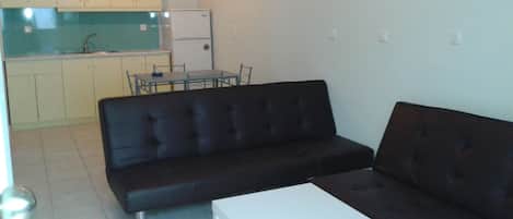 A living room with a black sofa, a white coffee table, and a kitchen area in the background.
