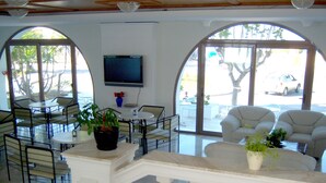 Un amplio espacio interior con balcón, amoblado con mesas y sillas, y un televisor montado en la pared.