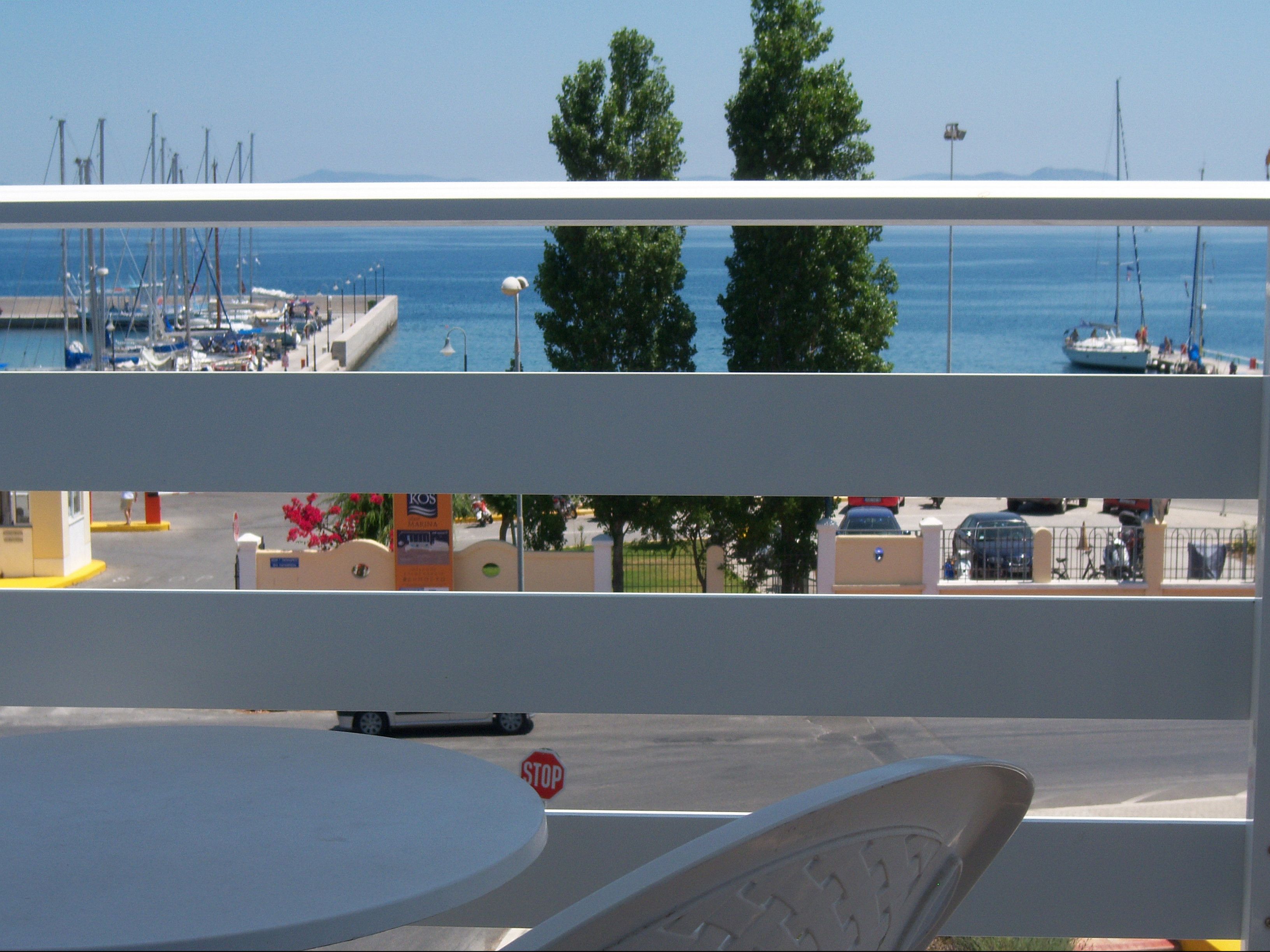 A view from a balcony overlooking a marina with boats, a stop sign, and a road with cars and a pedestrian.