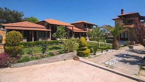A two-story house with a tiled roof, surrounded by well-maintained gardens and a paved driveway. - Kamelia Hotel (SARONIC ISLANDS)