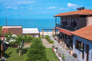 A coastal property with a balcony overlooking the sea, a garden with potted plants, and a building with a tiled roof. - Kamelia Hotel (SARONIC ISLANDS)