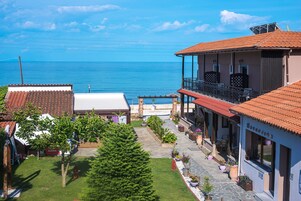 A coastal property with a balcony overlooking the sea, a garden with potted plants, and a building with a tiled roof.