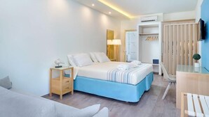 A modern hotel room with a large bed, a desk, a chair, and a wardrobe. - Kamelia Hotel (SARONIC ISLANDS)