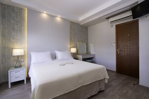 A hotel room with a bed, bedside tables, a mirror, a wardrobe, and an air conditioning unit.