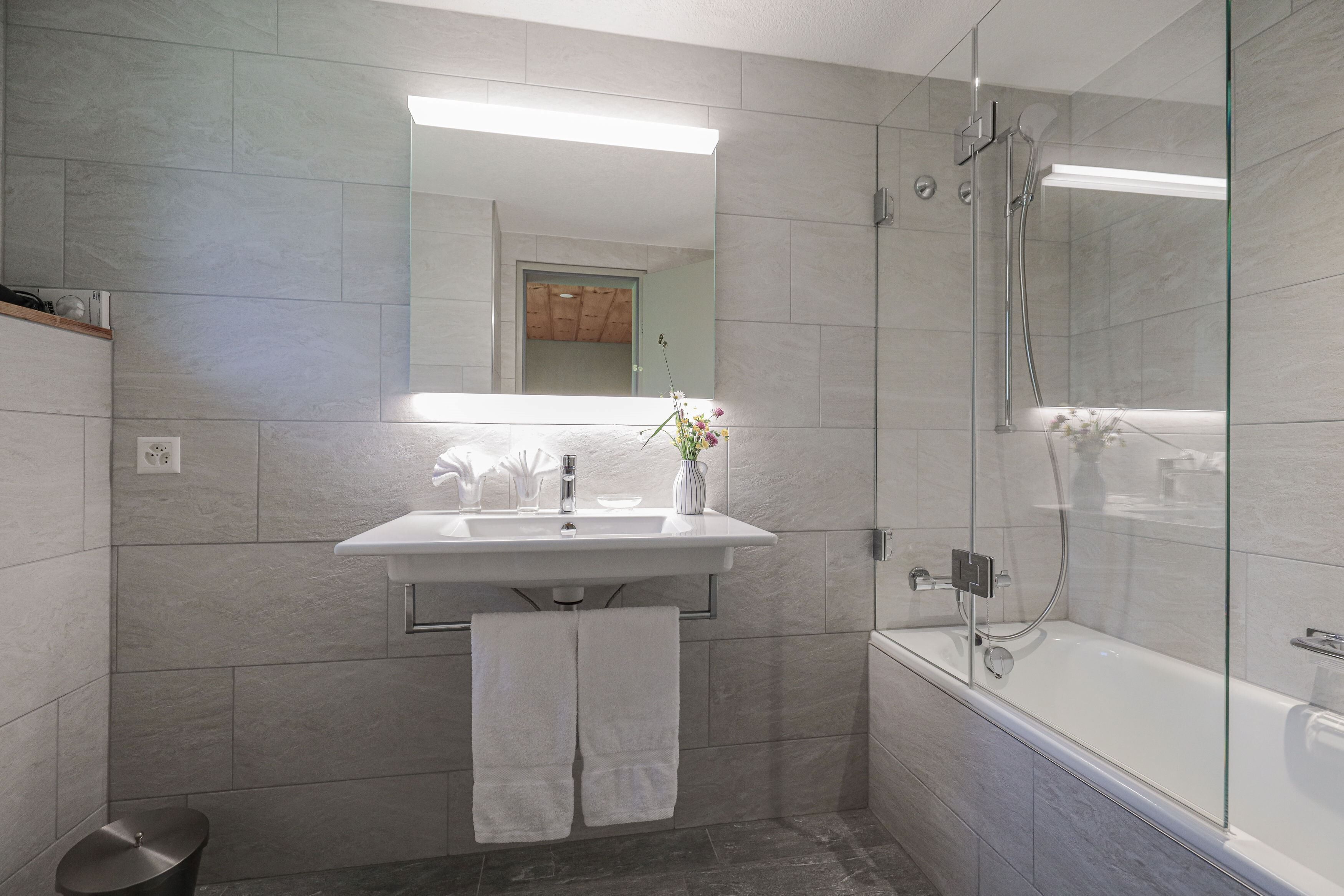 A modern bathroom with a glass-enclosed shower, a white sink, and a mirror above it.