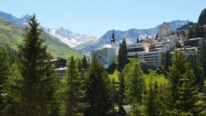 Un hotel con una torre destacada, rodeado de abundante vegetación y montañas al fondo.