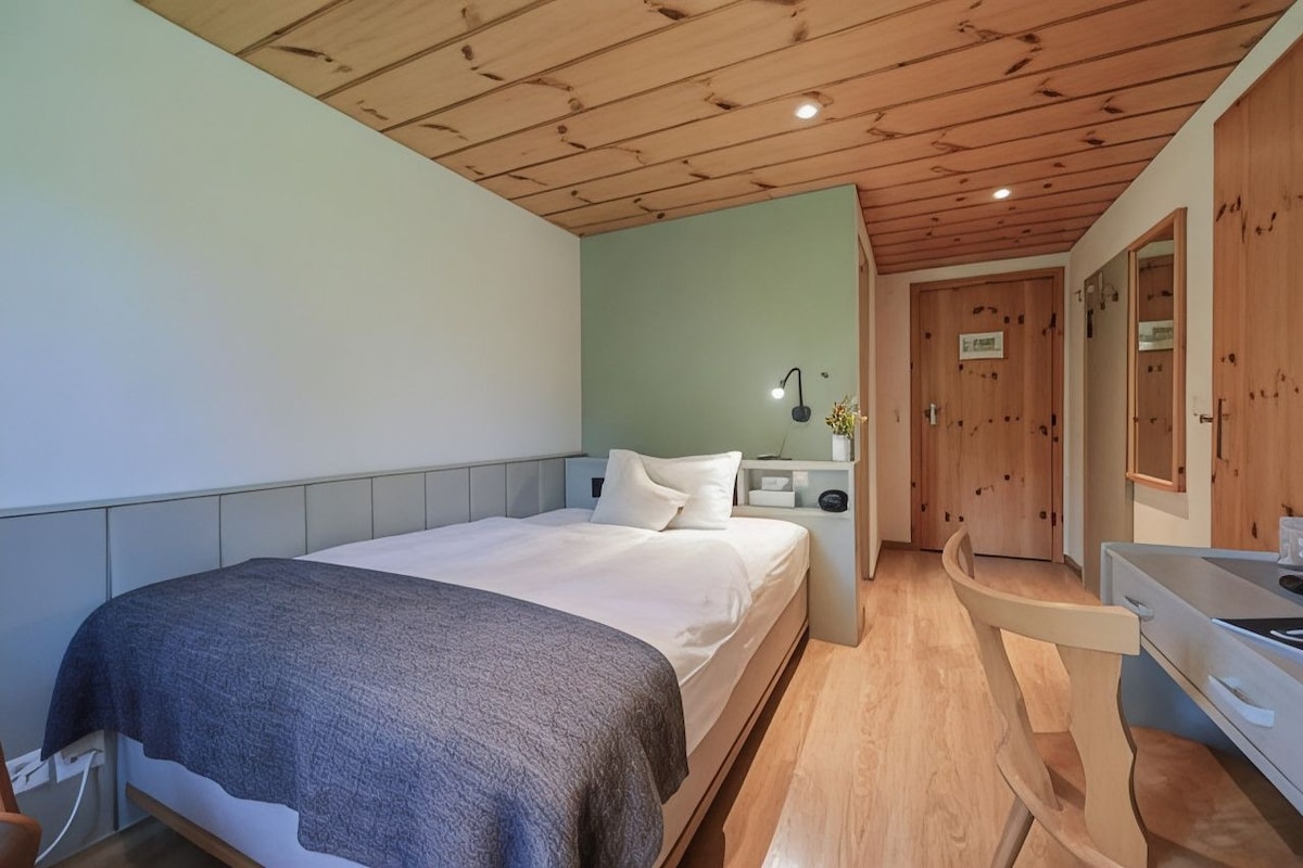 A bedroom with a bed, bedside table, lamp, and a mirror.
