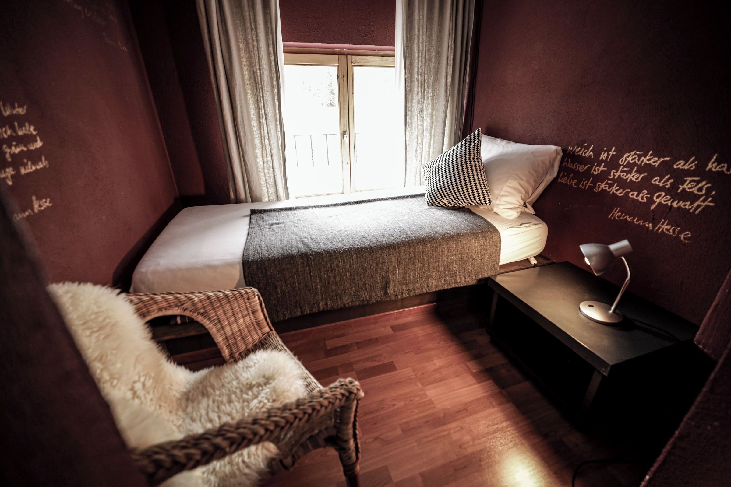 A cozy bedroom with a bed, a chair, a nightstand, and a window with curtains.