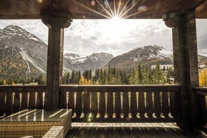 A wooden balcony with a glass table and bench, overlooking a mountainous landscape with snow-capped peaks and a forested area. - Hotel Seehof Arosa (Arosa)