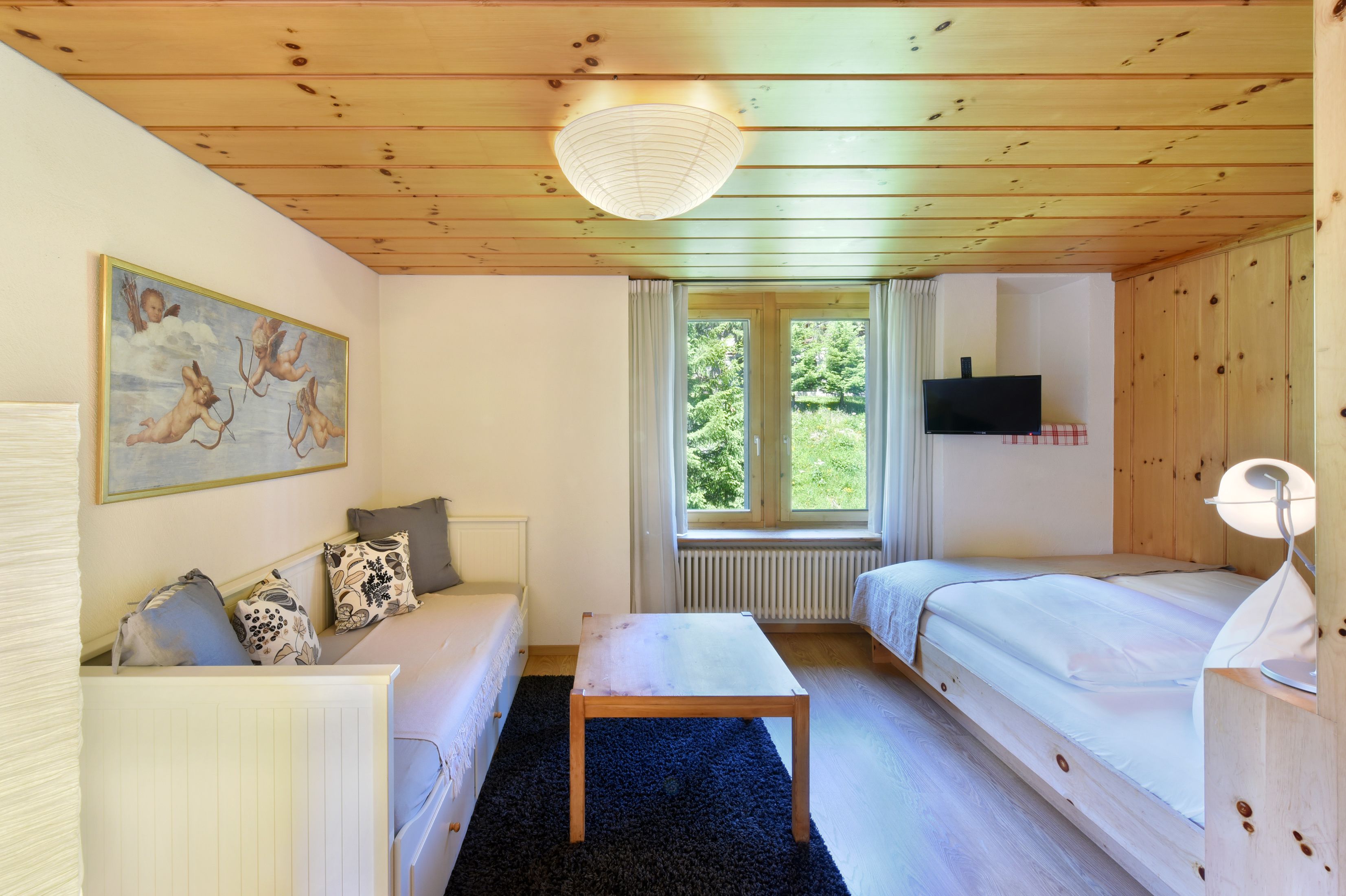 Een knus interieur met een houten plafond, een bed, een bank, een tafel en een schilderij aan de muur.