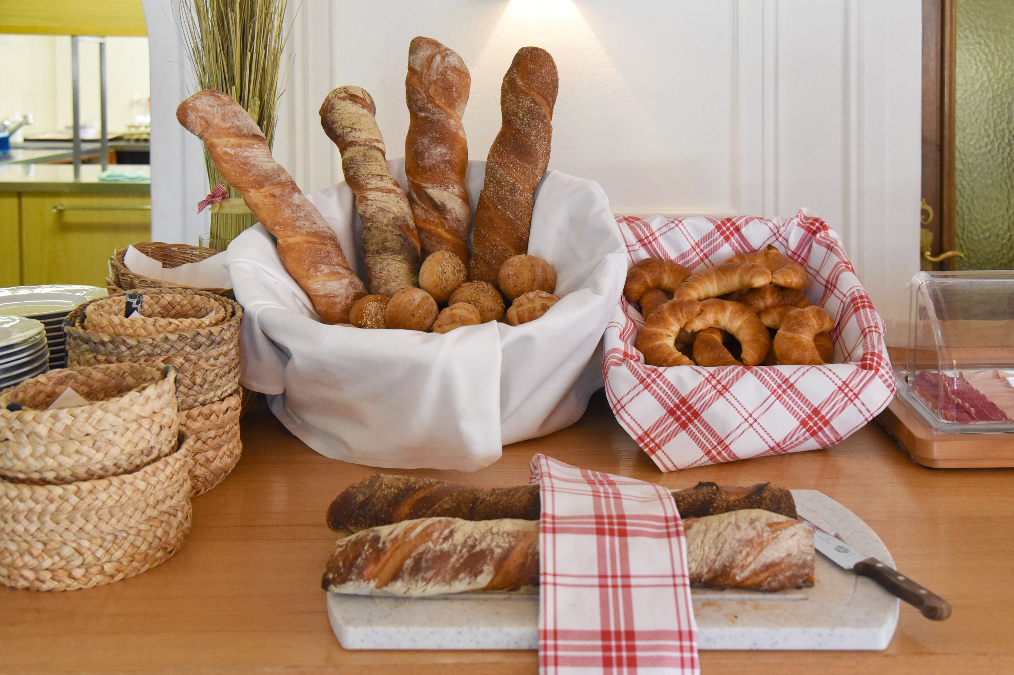 Variedad de panes y pasteles exhibidos sobre una mesa de madera, con cestas y una tabla de cortar.
