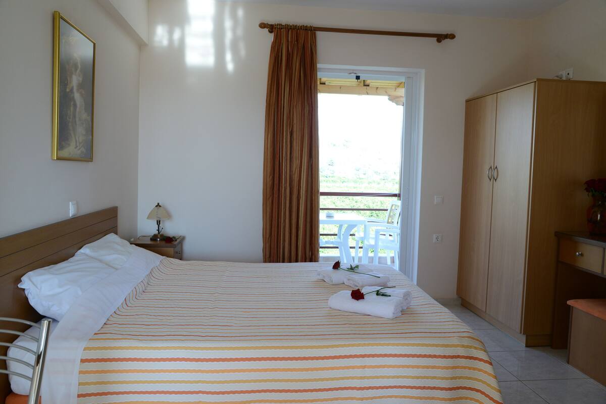 A hotel room with a bed, a nightstand, a wardrobe, and a view of the outdoors.