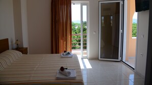 Habitación de hotel con cama, mesita de noche, televisión y balcón con vistas a la vegetación y montañas.