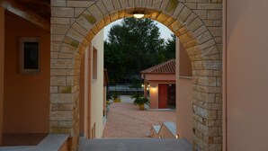 Un arco de piedra que conduce a un patio con techo de tejas, plantas en macetas y un edificio con puerta roja.