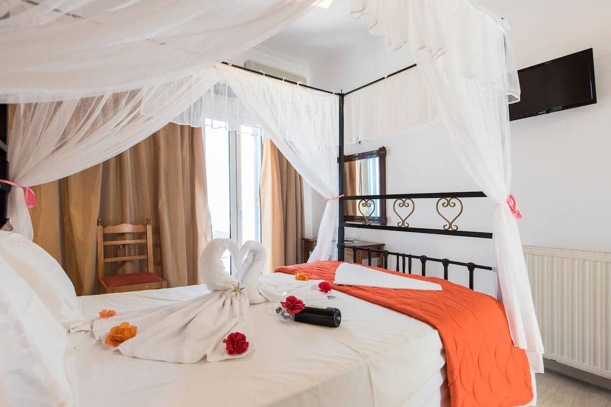 A hotel room with a bed, a TV mounted on the wall, and a window with curtains.