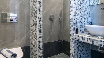 Un baño moderno con cabina de ducha revestida de mosaicos, un lavabo blanco y un inodoro.