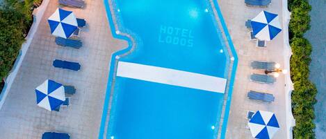 A swimming pool with a sign reading "HOTEL LODOS" surrounded by lounge chairs and umbrellas.