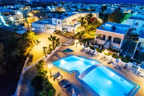 Un hotel con piscina, sillones de descanso y un espacio exterior bien iluminado.