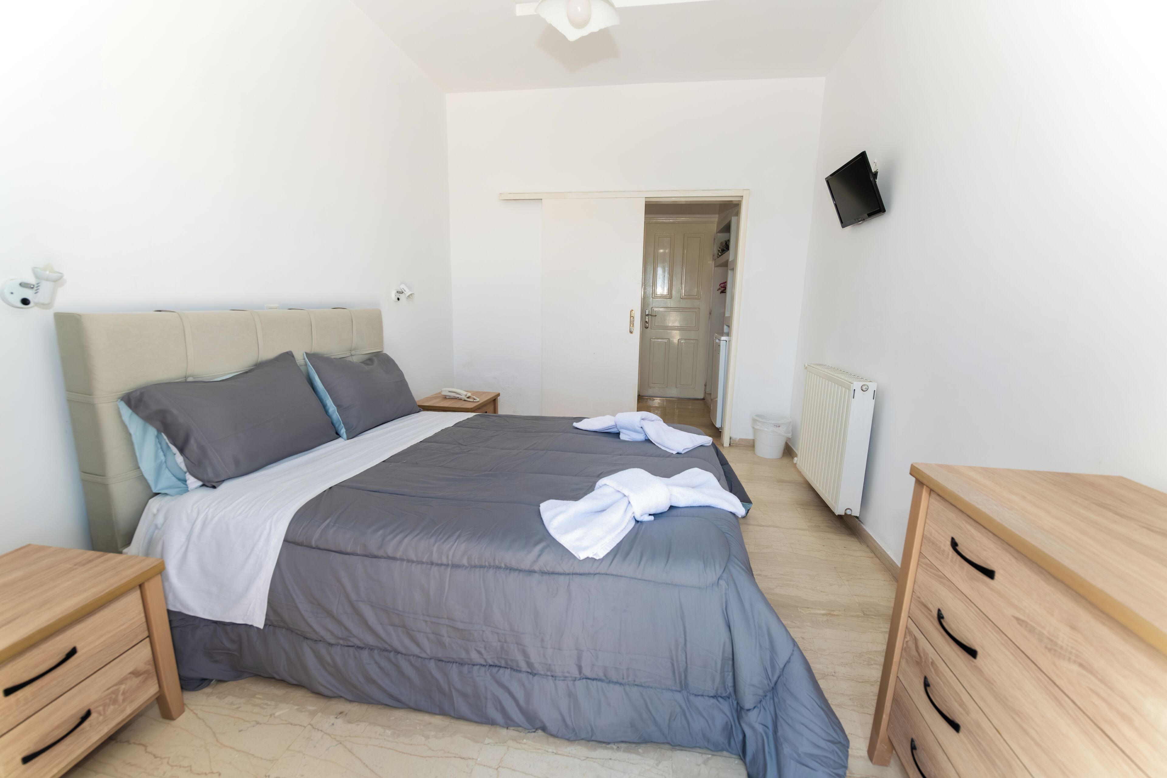 Une chambre à coucher avec un lit, des tables de chevet, une télévision et une porte.