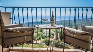 A balcony with a table, two chairs, a bottle of wine, and a glass. - Dianas Studios (Kefalonia)