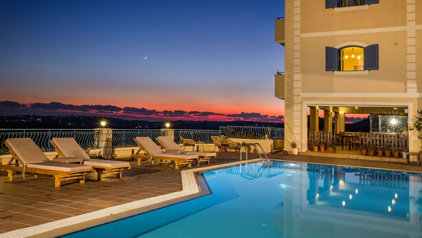 A rooftop pool area with lounge chairs and a bar, overlooking a sunset. - Dianas Studios (Kefalonia)
