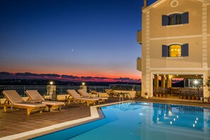 A rooftop pool area with lounge chairs and a bar, overlooking a sunset. - Dianas Studios (Kefalonia)