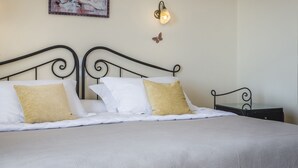 A neatly made bed with white and gold pillows, a wall-mounted light fixture, and a small decorative butterfly. - Dianas Studios (Kefalonia)