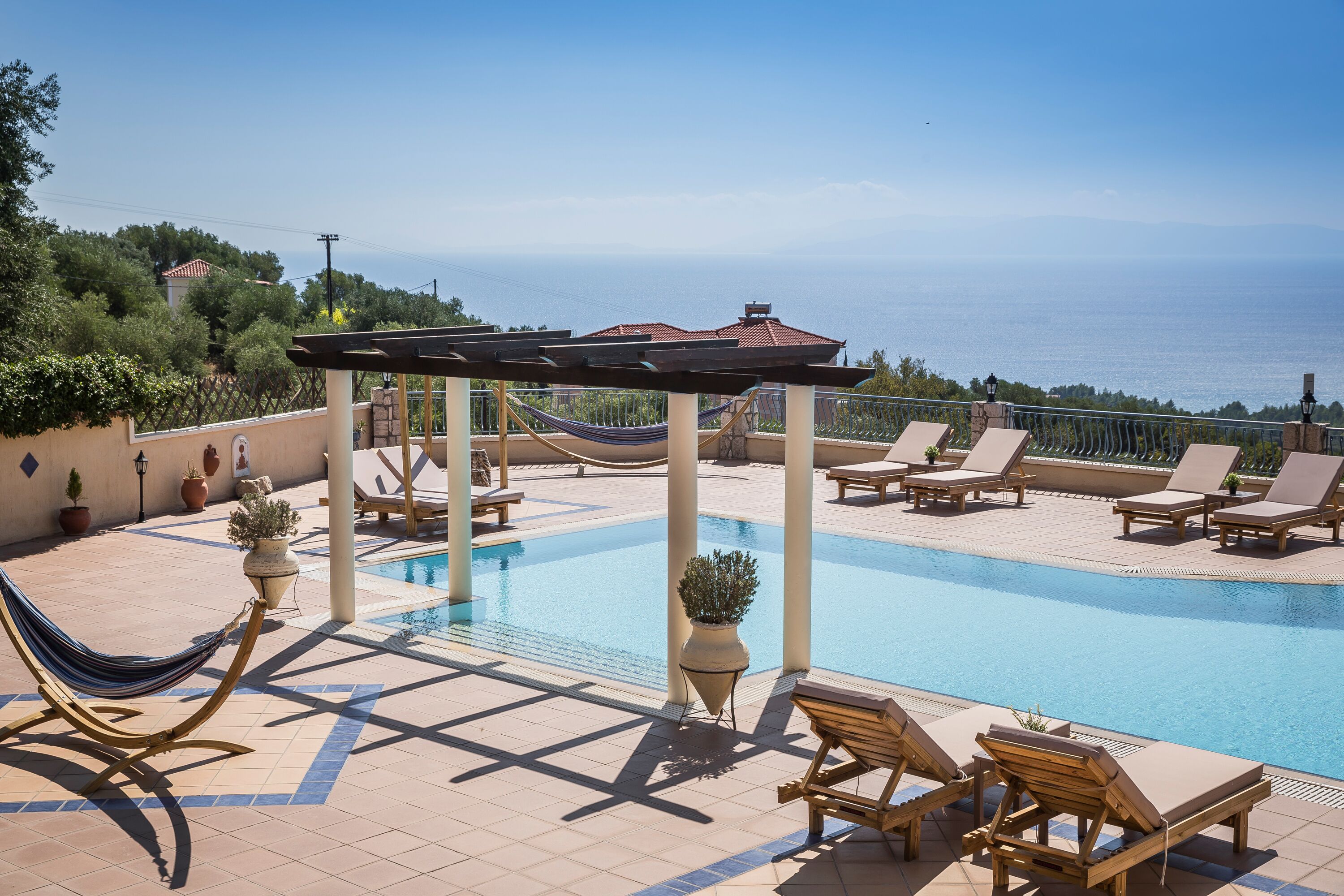 A pool area with lounge chairs, a hammock, and a pergola overlooking a body of water.